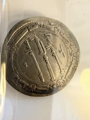 An Abbasid silver dirham featuring Arabic script and central dagger motifs.